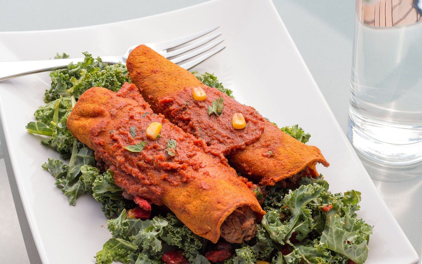 Blue-corn enchiladas stacked flat with red chile sauce and a fried egg on top, shot from above on a ceramic plate