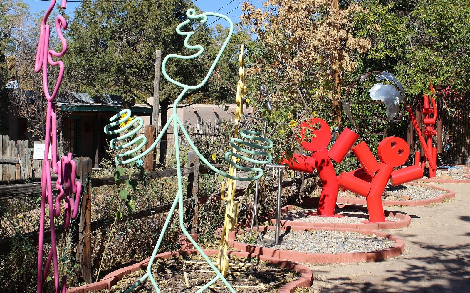 Colorful whimsical wire and metal sculptures line a garden path outside a gallery