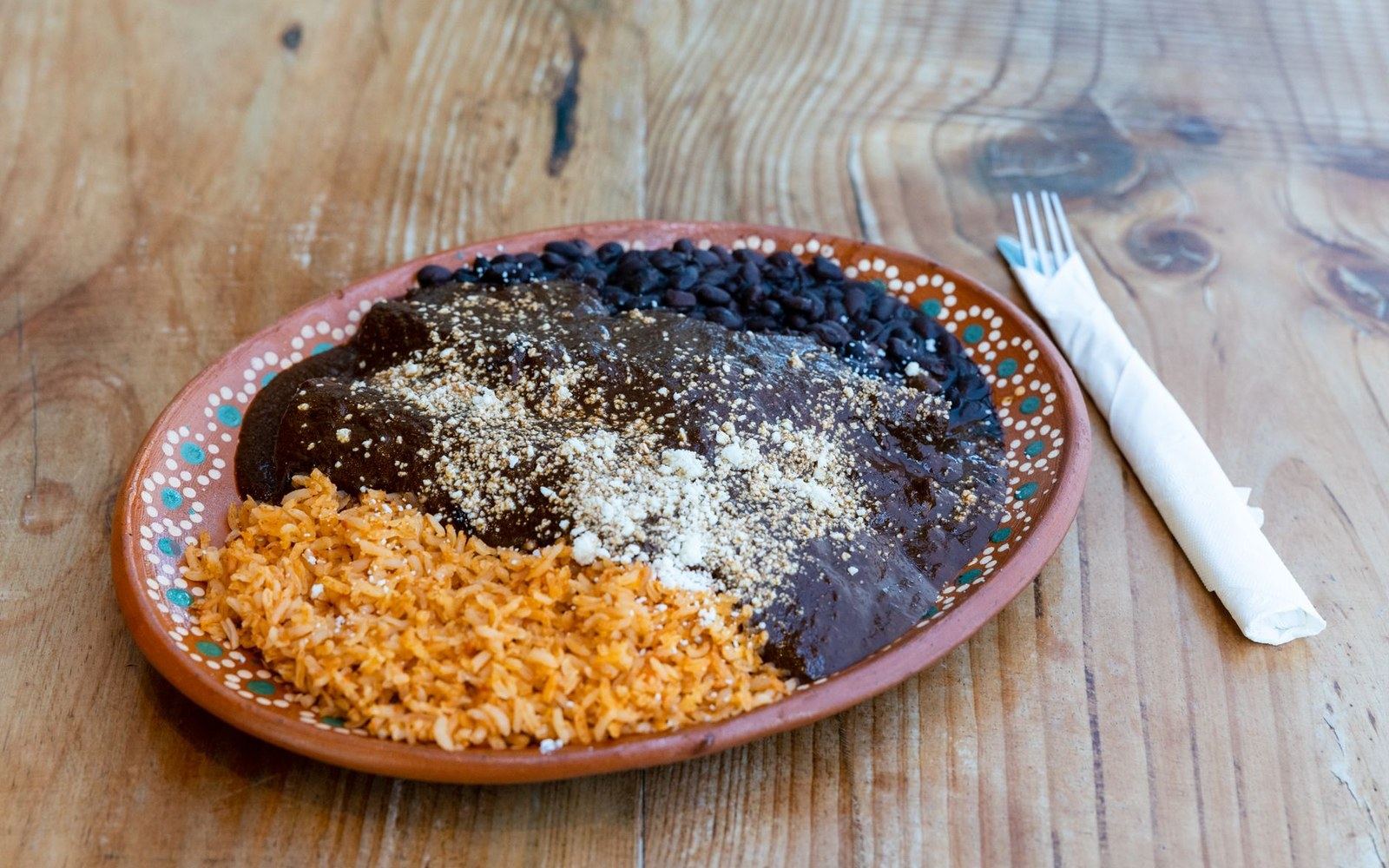 Plate of mole-covered enchilada with black beans and orange rice on a decorative dish