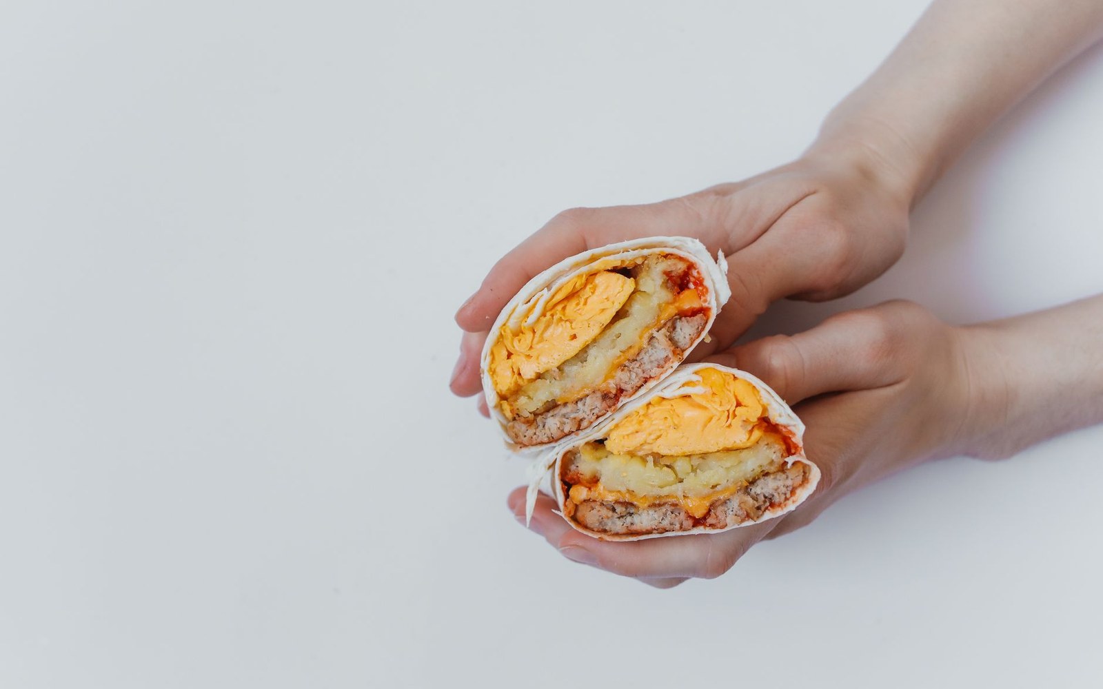 Two hands hold a burrito cut in half, revealing egg, sausage, cheese and potato layers