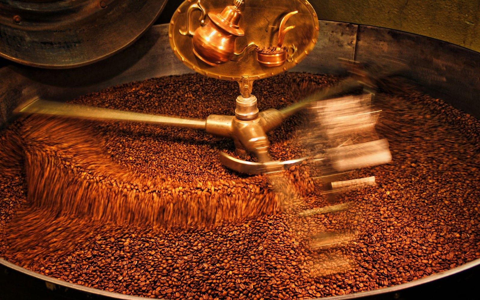 An adult roaster at the crank of a propane drum roaster, green chile mid-turn, smoke rising in September afternoon light