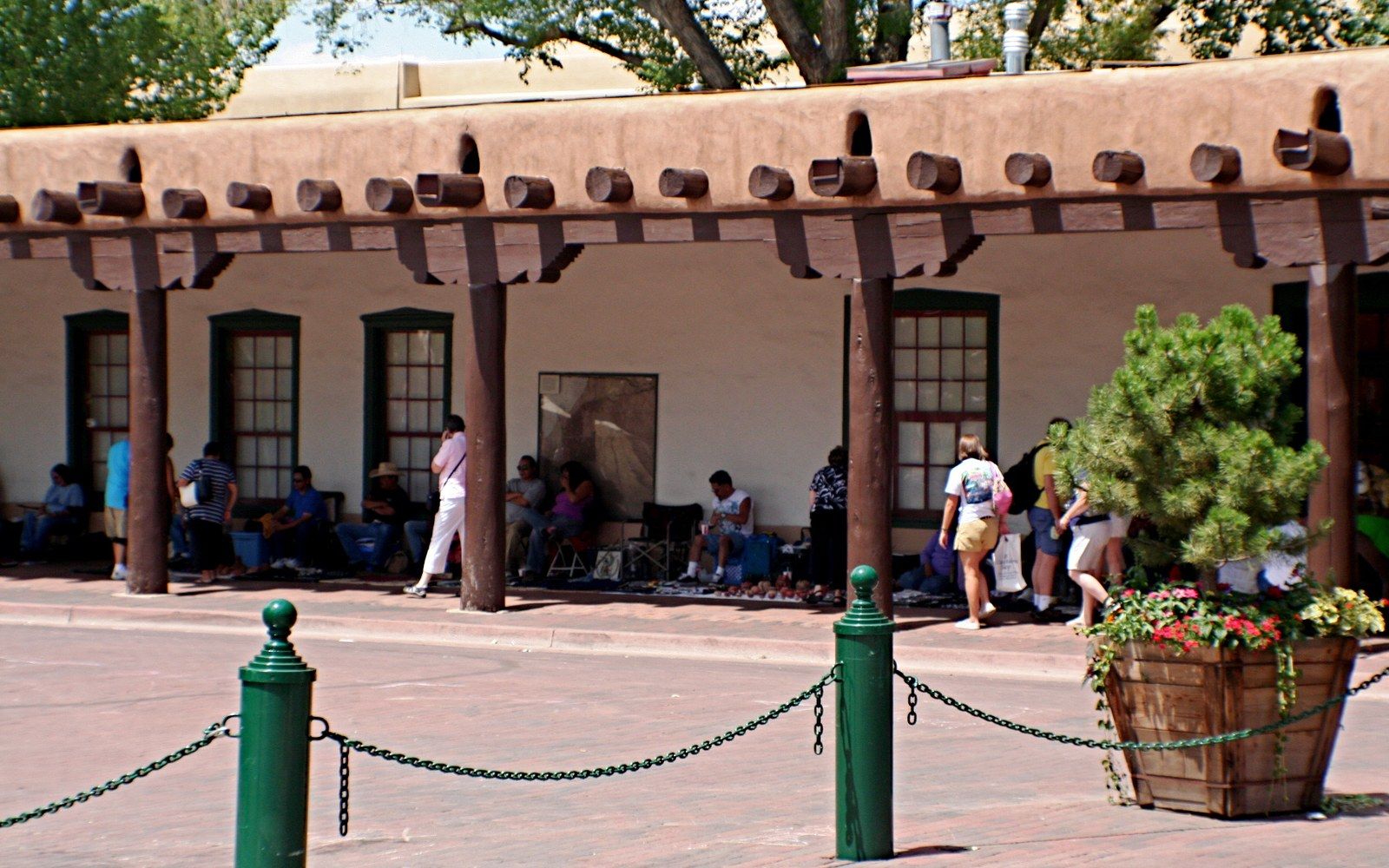 The portal of the Palace of the Governors on the Santa Fe Plaza, adult vendors behind blankets of jewellery, deep arcade shadow and bright light beyond